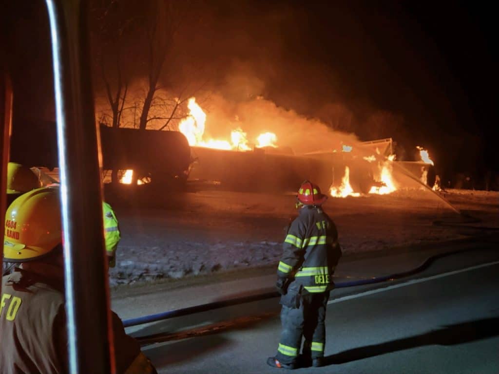 Rail safety laws are under increasing scrutiny with each new derailment. Here, firefighters look on as flames burst from a derailed train in Raymond, Minn.